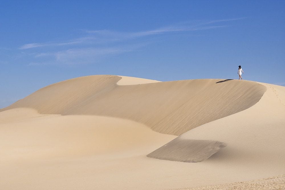 A woman walking along sand dunes.