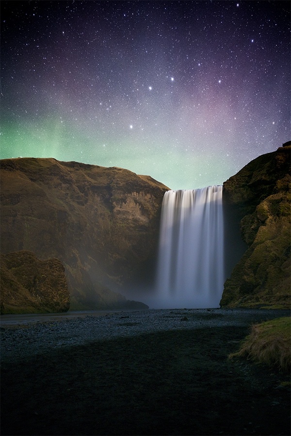 The Northern Lights dancing above a waterfall in Iceland 
