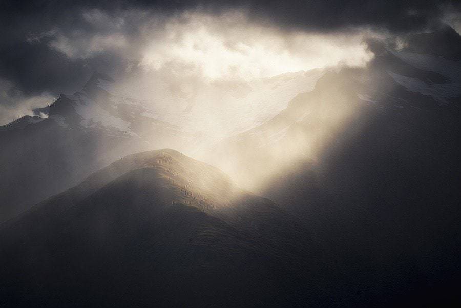 Sunlight beaming thorugh clouds on to a mountain