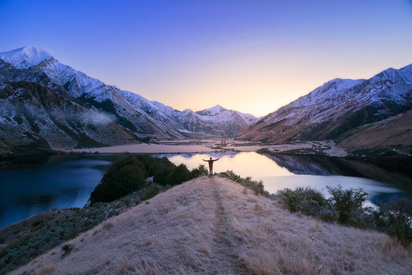 A man standing in front of a lake and snowy mountains